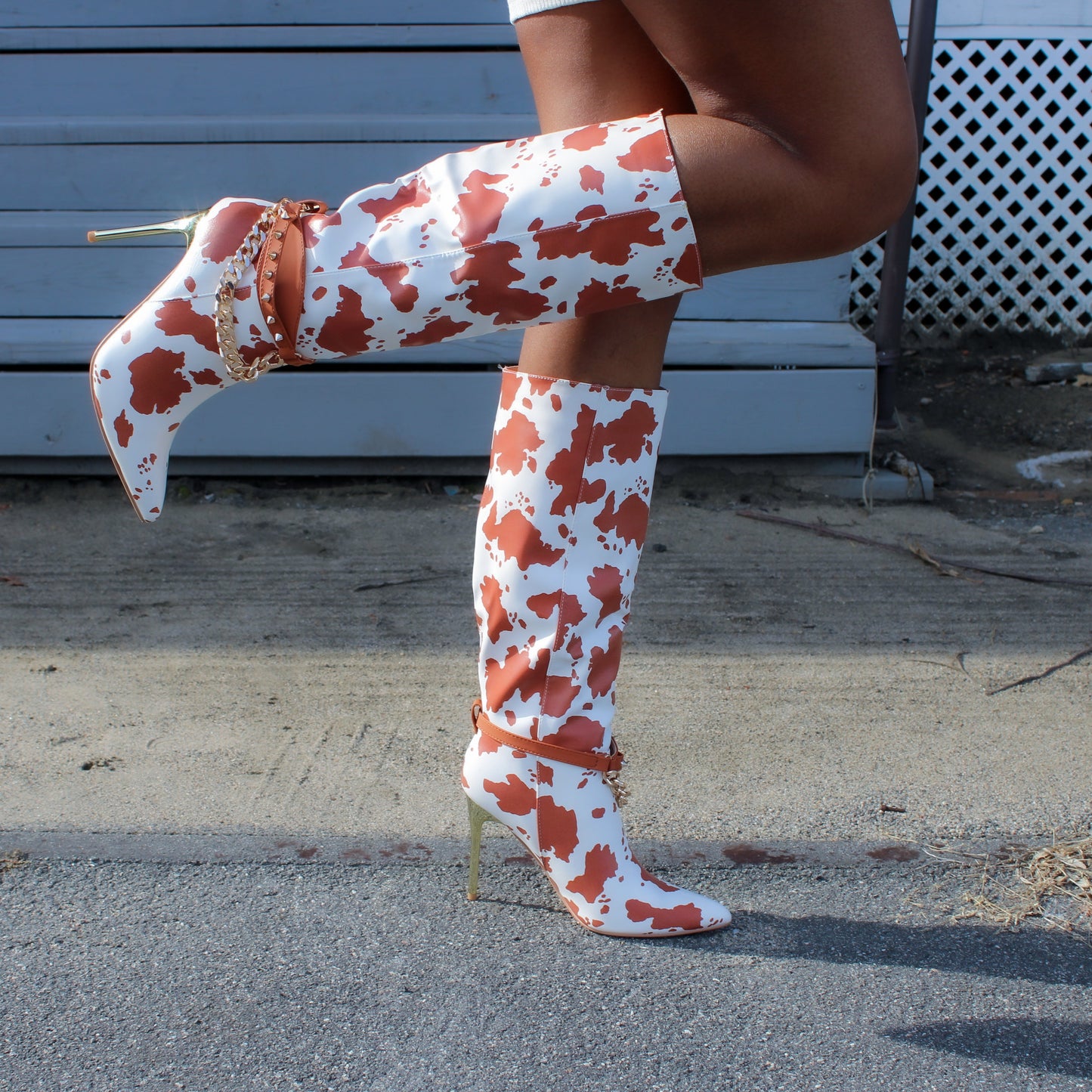 up close visual of cow print faux leather boots with gold spikes and chain accent