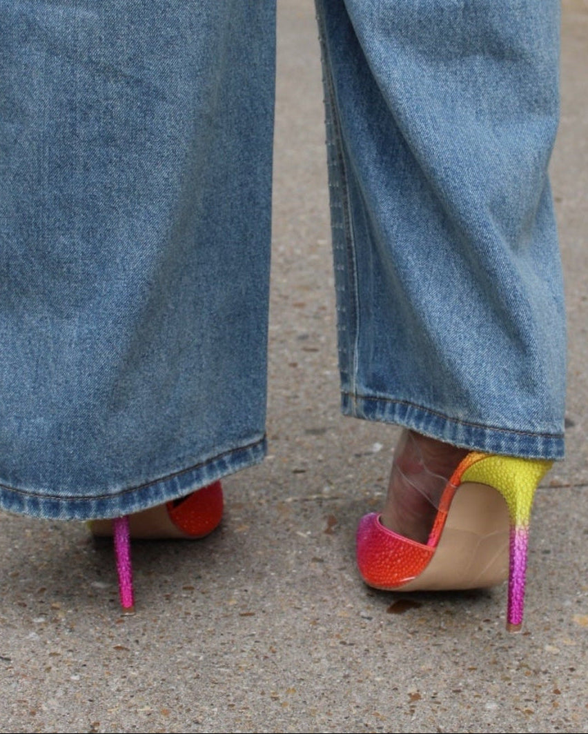 Close-up of wide-leg jeans with colorful high-heeled shoes on a concrete surface